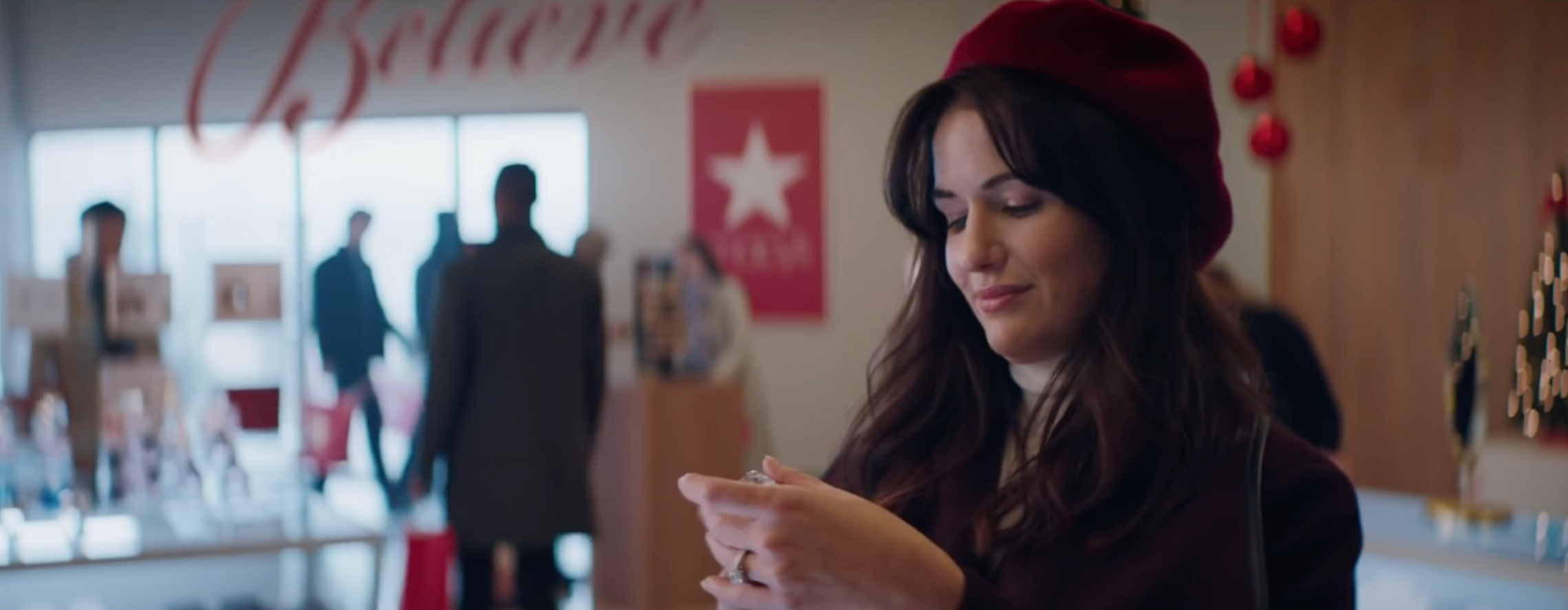Image of a white woman with brown hair and a red beret at a Macy's perfume counter. Christmas decorations fill the background.