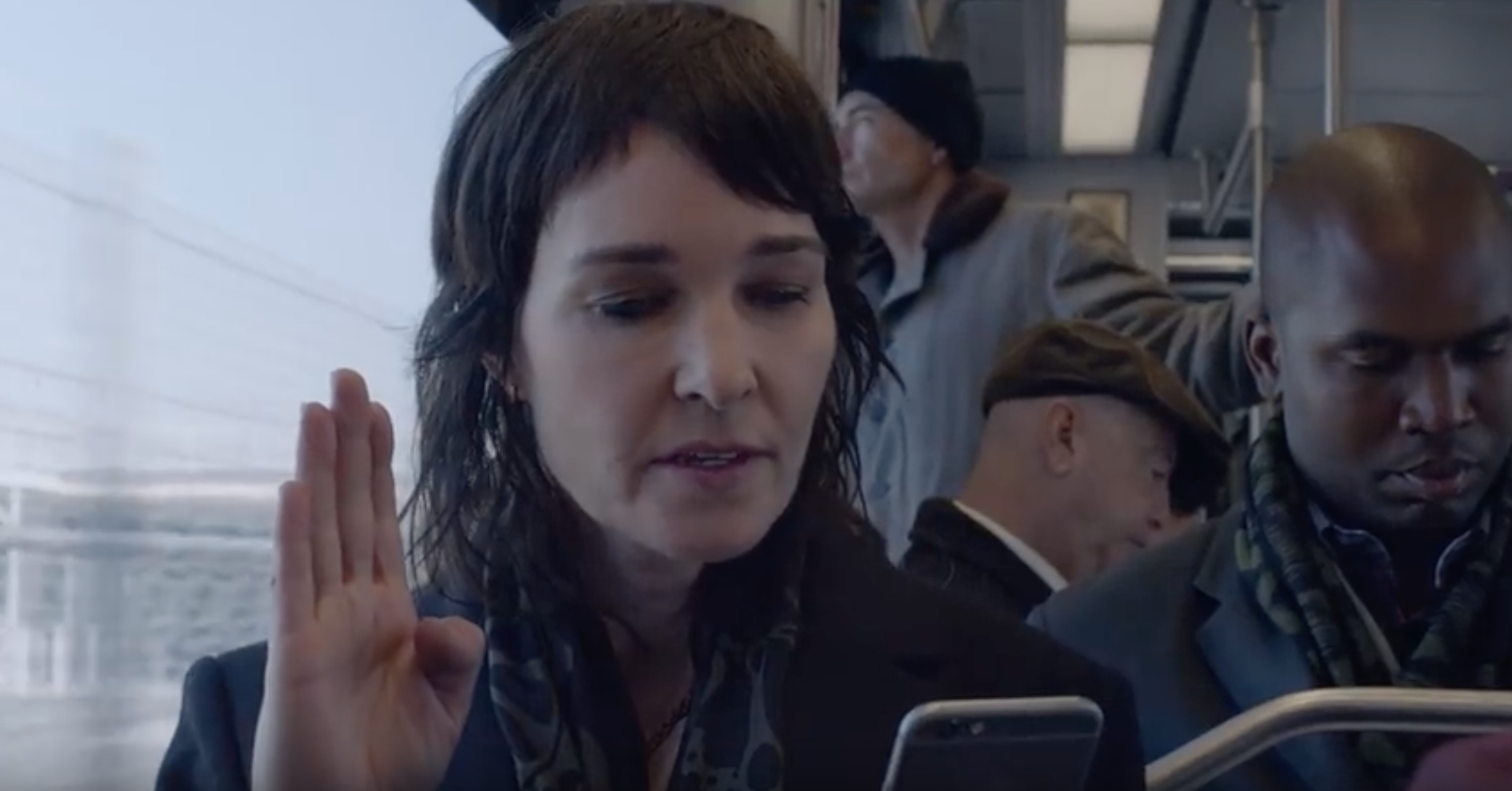 Image of a 30-something white woman with brown hair on a public bus, signing into her phone.
