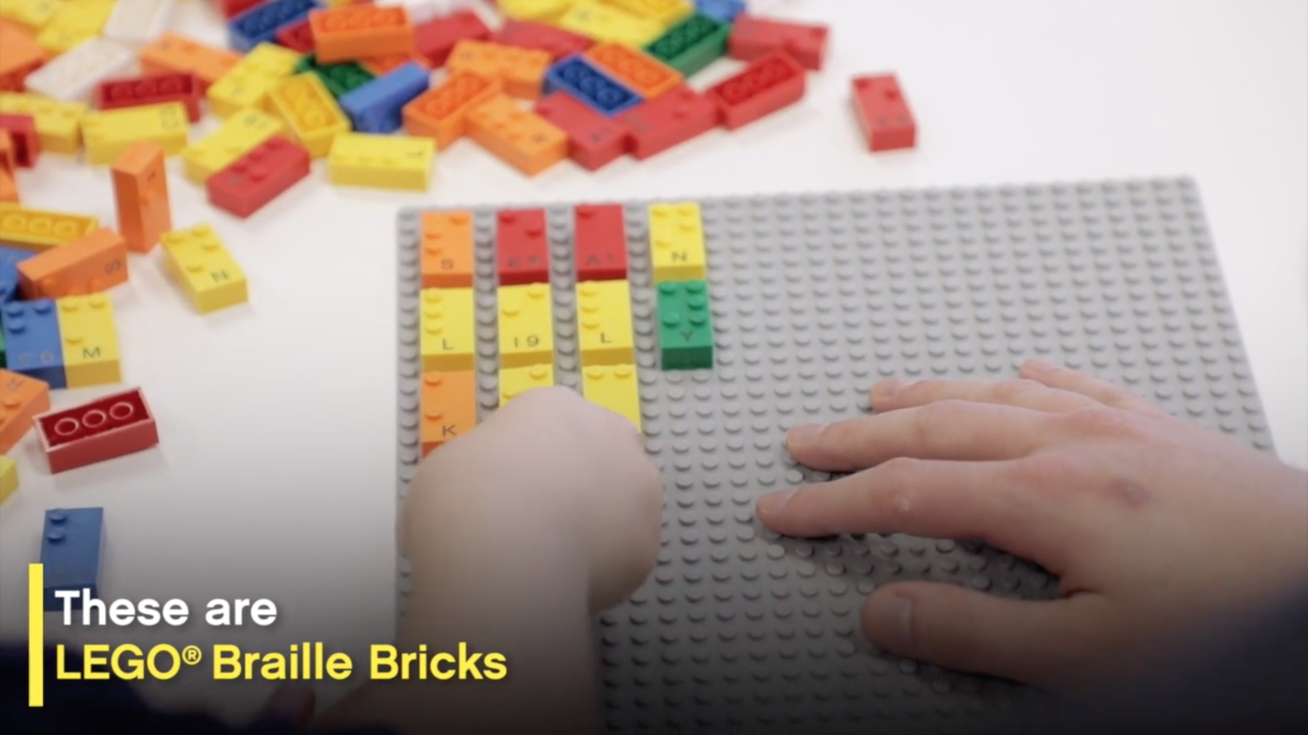 Image of a childs hand playing with LEGO Braille Bricks. It's a screenshot from the video.