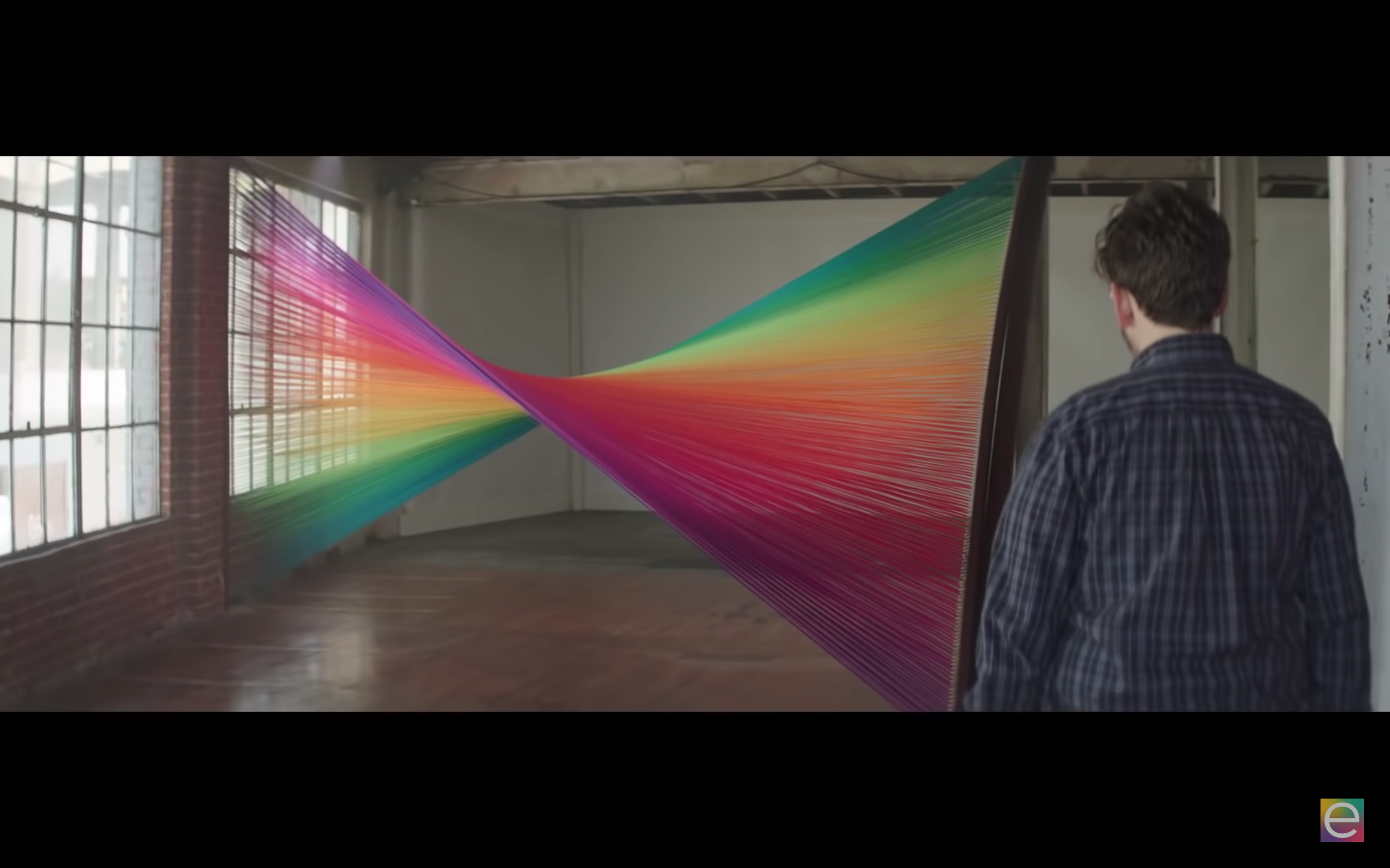 Image of a man standing in front of a large string rainbow colored installation inside a brightly lit room