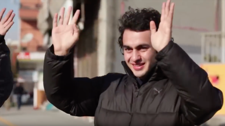 Image of a man, standing outdoors, with his hands in the air, signing applause.