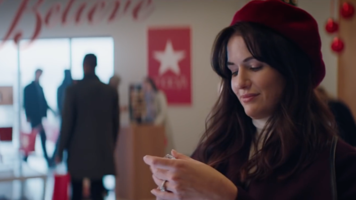 Image of a white woman with brown hair and a red beret at a Macy's perfume counter. Christmas decorations fill the background.