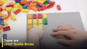 Image of a childs hand playing with LEGO Braille Bricks. It's a screenshot from the video.