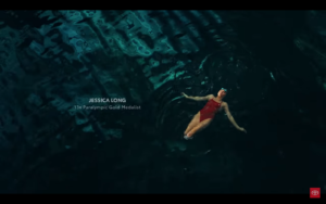 Image from the beginning of the ad. Jessica Long, a double amputee wears a red swimsuit while swimming in dark water. White text on the screen tells us she's a 13x paralympic gold medalist